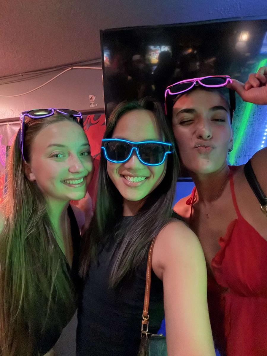 Three friends with purple, blue and pink Sunglasses At Night LED glasses pushed up on their heads