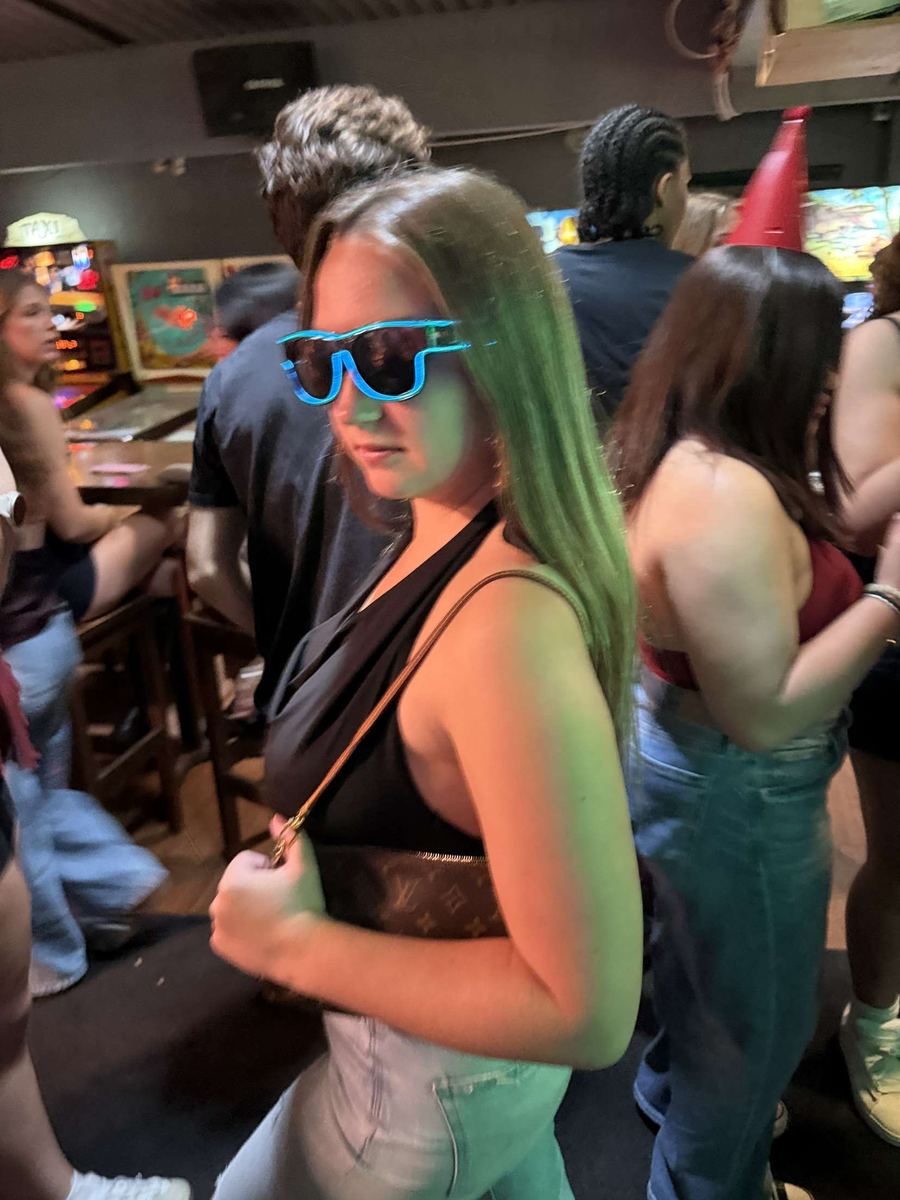 Woman wearing blue Sunglasses At Night LED glasses on a busy bar floor